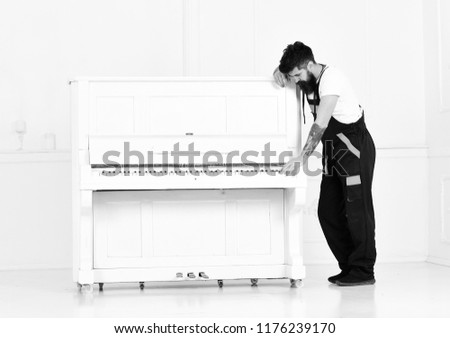 Strong bearded man moving old wooden piano with open keyboard isolated on white background. Handsome guy playing easy tune on pianoforte.