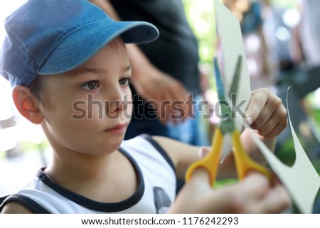Boy cuts out figure with scissors from sheet of paper