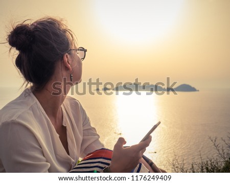 Young woman using smartphone at sunset in front of the sea on Ponza island coast