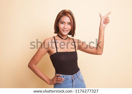 Young Asian woman smile and point on beige background