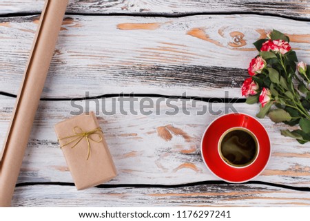 Cup of coffee, flowers and a gift wraped in a paper. Top view, flat lay. Old white wood background.