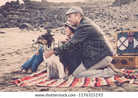 happy couple with nice dogs stay at the beach doing picnic enjoyng the nature and the relationship. vintage colors and filter for romantic and travel concept image. different lifestyle adult people