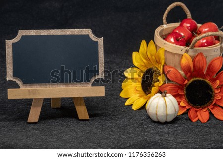 Beautiful fall and autumn scene with a basket of apples, colorful sunflowers and blank chalkboard for your text message. Black background