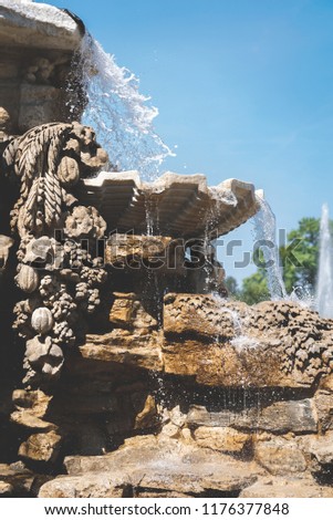 Photo of a stone architectural construction of the fountain. Drops and streams of water flow on red
