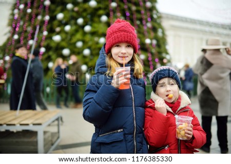 Two adorable sisters drinking hot apple juice on traditional Christmas market. Child enjoying sweets, candies and gingerbread on magical Xmas time.