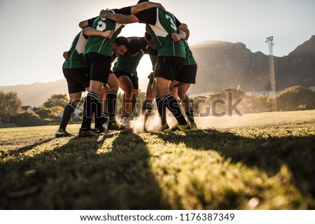Rugby players in a huddle rubbing their feet on grass. Rugby team showing aggression after the win. Royalty-Free Stock Photo #1176387349