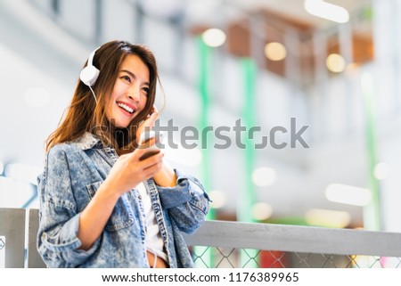 Beautiful young Asian girl listen to music using smartphone and headphone smile at copy space. Modern teenager lifestyle, college student hobby, youth culture or mobile phone gadget technology concept Royalty-Free Stock Photo #1176389965