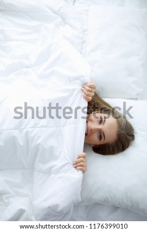 Face closeup of a beautiful young woman hiding her face under the sheet Royalty-Free Stock Photo #1176399010