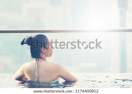 Young woman in a roof top swimming pool with beautiful city view, sunlight vintage filter image
