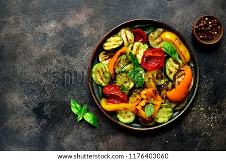 Grilled vegetables (  colorful bell pepper, zucchini, eggplant ) with basil and dry herbs on a plate over dark slate, stone, concrete or metal background.Top view. Royalty-Free Stock Photo #1176403060