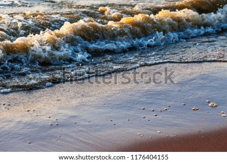 Waves on the sandy shore of a large river. The rays of light are reflected in the waves,