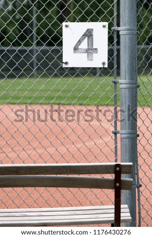 The Number Four on a Chain Link Fence by a Bench at a Baseball Field