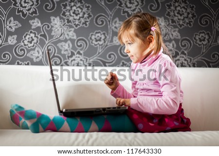 Pretty young blond girl sitting on a sofa using her laptop computer and thinking carefully about the next step.