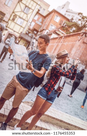 Stylish woman taking photo of city while man with map standing near and both smiling