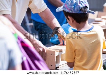 Young boy child with a hammer building bird treehouse with a help of an adult.