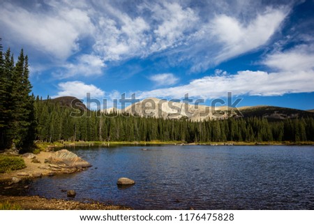A photo of Brainard Lake in Colorado with well interesting lighting on the mountains in the background and intense clouds in the sky. 