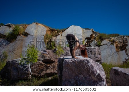 A red-haired young woman in brown overalls is engaged in pilates on the edge of an abandoned marble quarry. A girl practices yoga alone in a place of marble extraction.