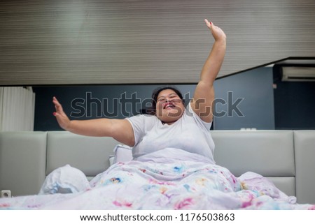 Picture of obese woman stretching hands in the bed after wake up. Shot at home
