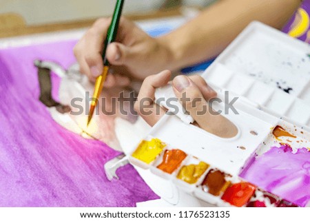 closeup hands holding brush and colored palette with watercolor paints by artist painting