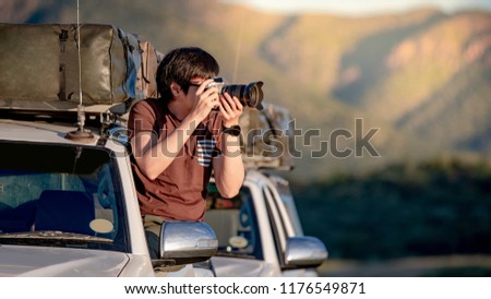 Young Asian mle traveler and photographer sitting on the car window taking photo on road trip in Namibia, Africa. Travel photography concept