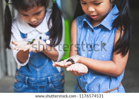 Two cute asian child girls holding and playing with black caterpillar with curious and fun together.