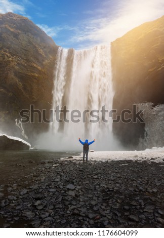 Backpacker Hiker man standing in front of huge waterfall skogafoss in iceland.