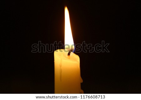 lone wax burning candle with big fire on dark background.