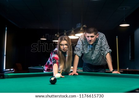 Young and beautiful couple playing billiard in bar
