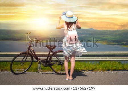 woman traveler standing beside bicycle near the lake background is mountain on vacation.young lady tourist enjoying for nature when the sunset.