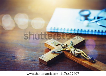 The crucifix and note book with stethoscope  on a doctor desk at hospital, Christian background with copy space, spiritual healing concept 