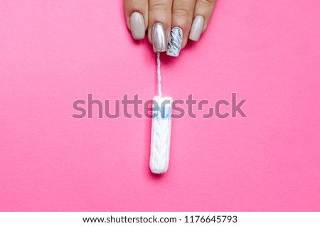 
woman with beautiful manicure holds a white tampon on a pink background