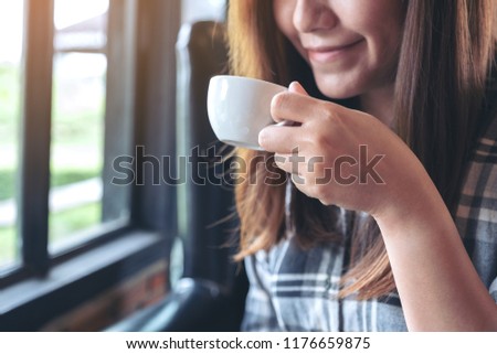 Closeup image of an asian woman holding and drinking hot coffee with feeling good in cafe