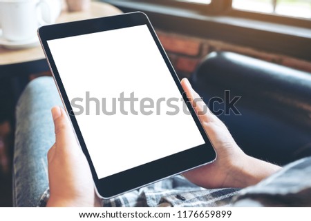 Mockup image of hands holding black tablet pc with blank white desktop screen while sitting in cafe