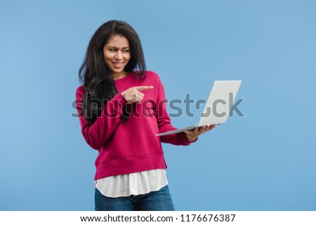 skeptical young african american woman pointing at laptop isolated on blue background 