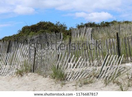 Moody picture of sand dunes, broken fencing blue skies and shrubs on a warm Summer day at the beach, long before people come to enjoy the day.