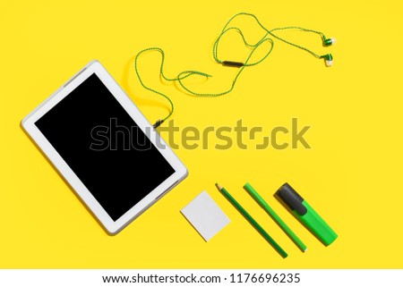 set of business gadgets and accessories from the top view. green pencils, headphones, paper stickers, markers and tablet pc lying on a yellow background. free space for advertising text