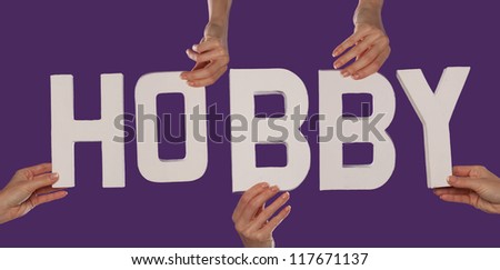 White alphabet lettering spelling HOBBY held up over a purple studio background by outstreched female hands