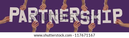 White alphabet lettering spelling PARTNERSHIP held up over a purple studio background by outstreched female hands