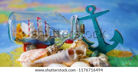 sailboat inside glass bottle, wooden blue anchor and many sea shell on paper world map background. 