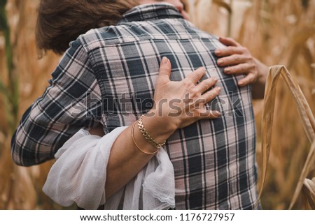 A mother hugs her adult son in the autumn field with dry corn leaves.. Maternal older hands closeup. The man in the plaid shirt. No faces. Royalty-Free Stock Photo #1176727957