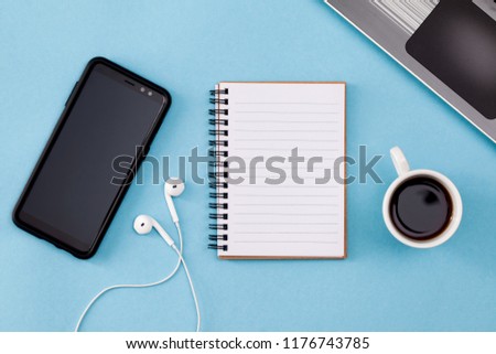 Modern blue office desk table with closed laptop, blank notebook page, pen, cup of coffee and headphones for input the text. Top view, flat lay. Freelancer workplace concept