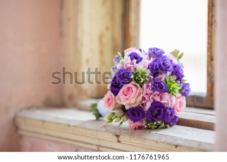 Pink an purple roses wedding bouquet placed in the frame of old vintage window, closeup photo of bridal flowers taken at daytime