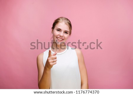 Horizontal portrait happy young girl showing a finger at you, white skinned female model at pink wall isolated.