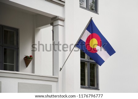 Colorado flag. Colorado state flag hanging on a pole in front of the house. State flag waving on a home displaying on a pole on a front door of a building. Flag raised at a full staff.