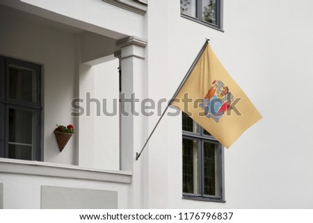 New Jersey flag. New Jersey state flag hanging on a pole in front of the house. State flag waving on a home displaying on a pole on a front door of a building. Flag raised at a full staff.