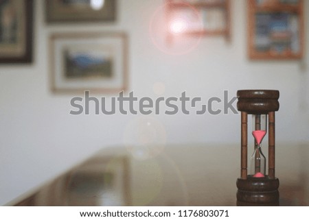 A close-up shot of a brown hourglass on a living room table. The picture frame on the wall is the background selective focus and shallow depth of field
