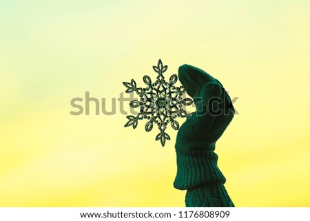 Female hands in a knitted mittens with sparkling huge snowflake on a sunset sky background. Winter and Christmas concept.