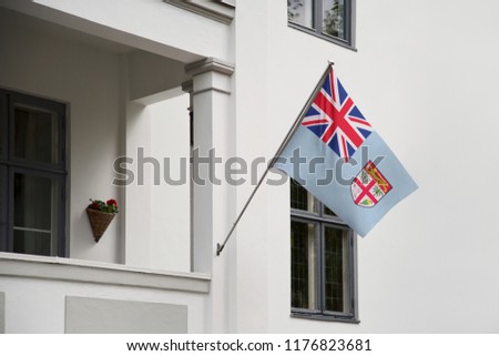 Fiji flag. Fijian flag hanging on a pole in front of the house. National flag waving on a home displaying on a pole on a front door of a building. Flag raised at a full staff.