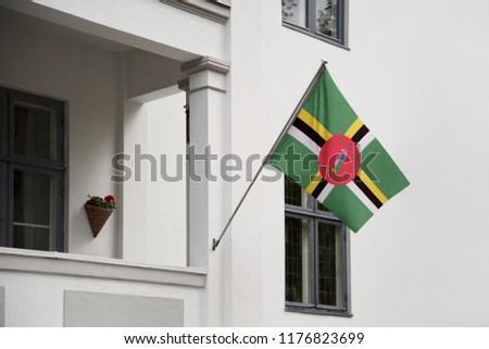 Dominica flag. Dominican flag hanging on a pole in front of the house. National flag waving on a home displaying on a pole on a front door of a building. Flag raised at a full staff.
