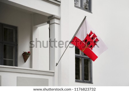 Gibraltar flag. Gibraltar flag hanging on a pole in front of the house. National flag waving on a home displaying on a pole on a front door of a building. Flag raised at a full staff.